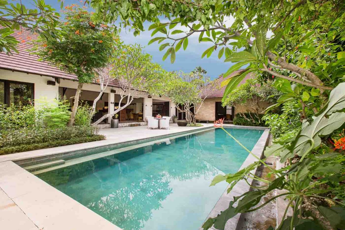 Modern luxury bathroom with freestanding white bathtub, glass shower enclosure, towels, and tropical plant accents. - Bali Villas