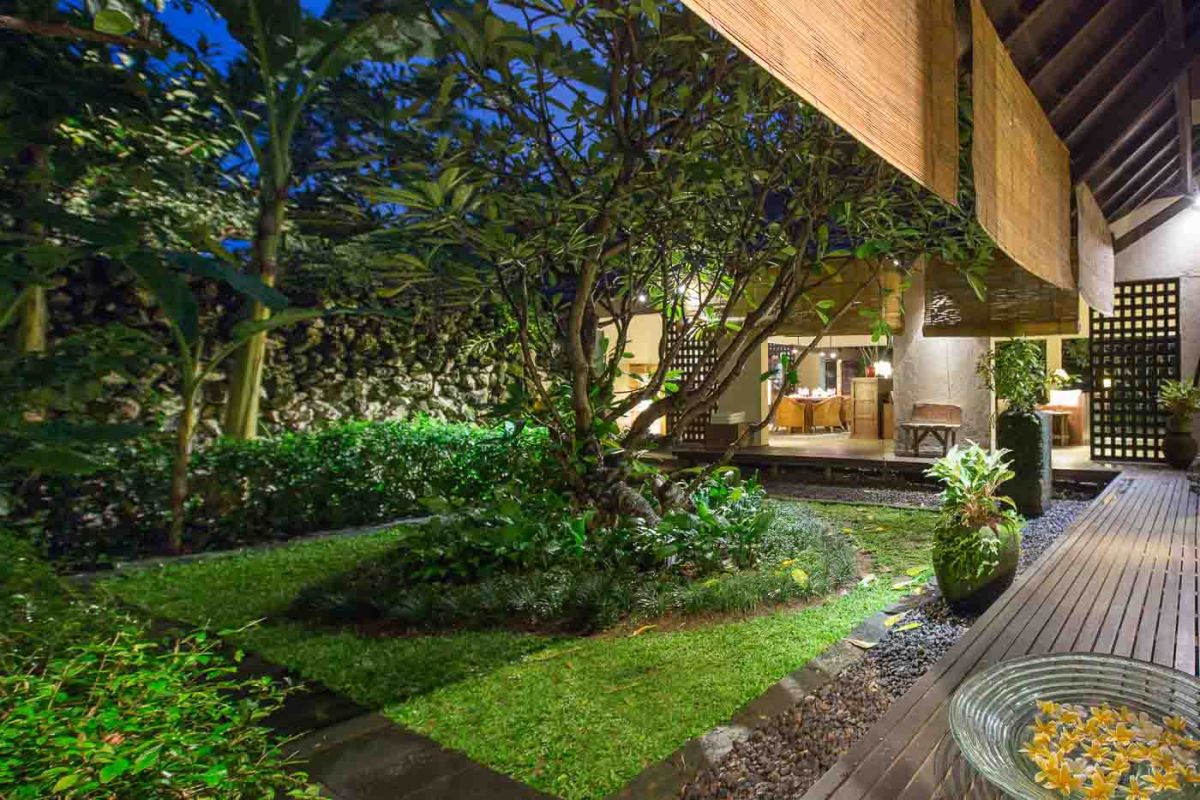 Modern luxury bathroom with freestanding white bathtub, glass shower enclosure, towels, and tropical plant accents. - Bali Villas
