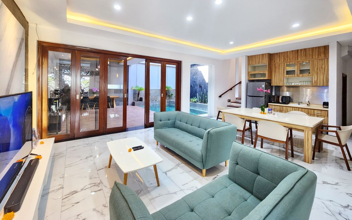 Modern open-plan kitchen and dining area with wooden cabinets, marble-top table, stainless steel fridge, and potted orchids in a Balinese villa. - Bali Villas