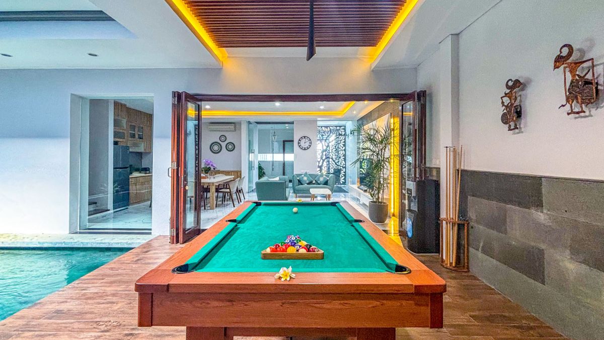 Modern open-plan kitchen and dining area with wooden cabinets, marble-top table, stainless steel fridge, and potted orchids in a Balinese villa. - Bali Villas