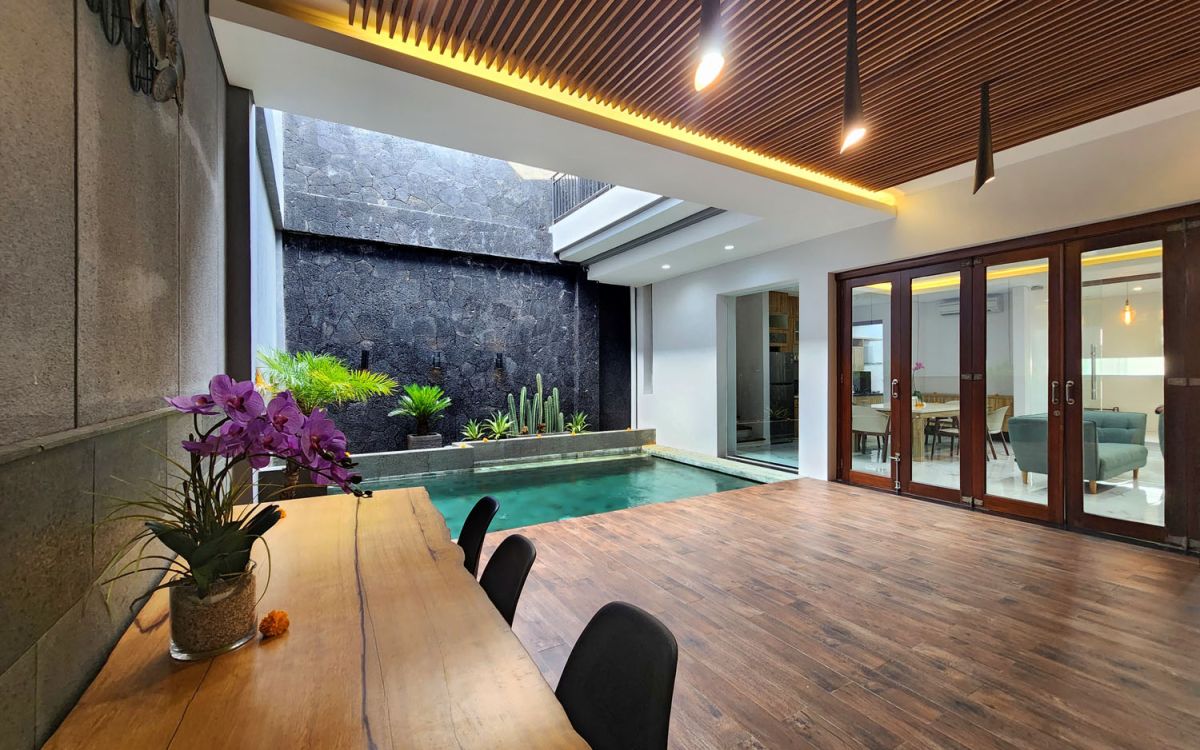 Modern open-plan kitchen and dining area with wooden cabinets, marble-top table, stainless steel fridge, and potted orchids in a Balinese villa. - Bali Villas