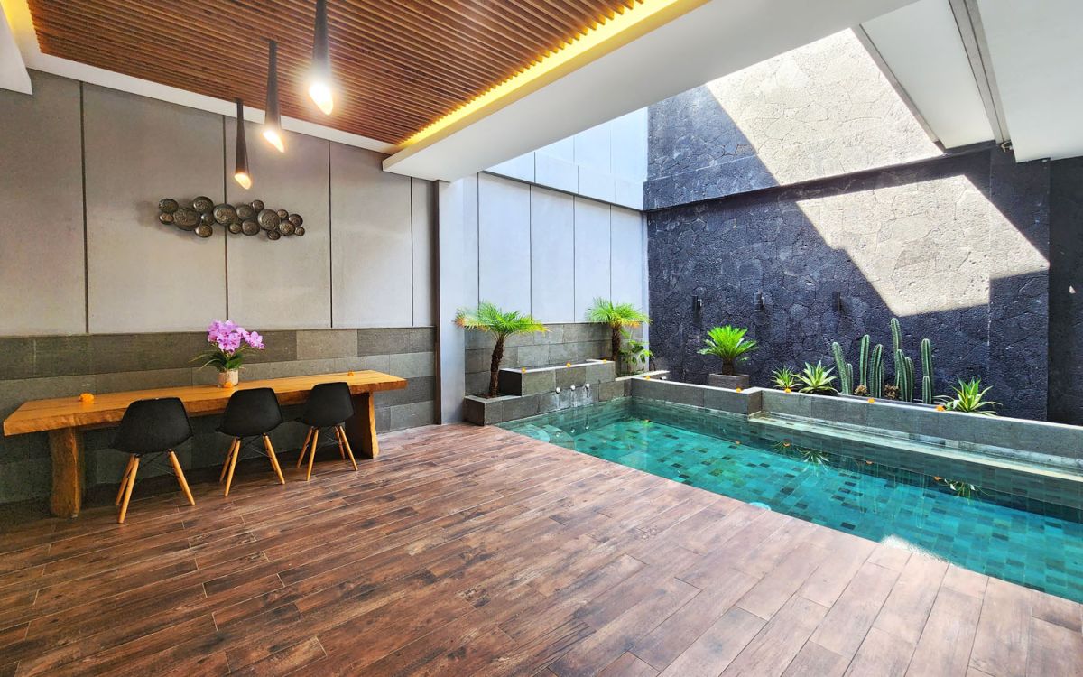 Modern open-plan kitchen and dining area with wooden cabinets, marble-top table, stainless steel fridge, and potted orchids in a Balinese villa. - Bali Villas