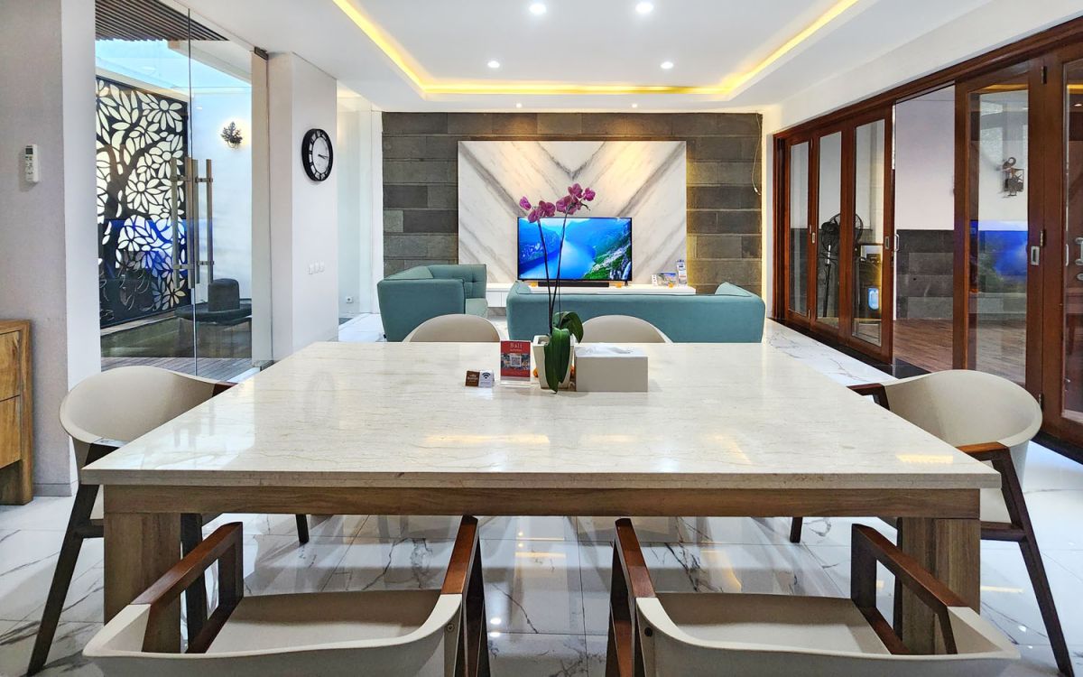 Modern open-plan kitchen and dining area with wooden cabinets, marble-top table, stainless steel fridge, and potted orchids in a Balinese villa. - Bali Villas
