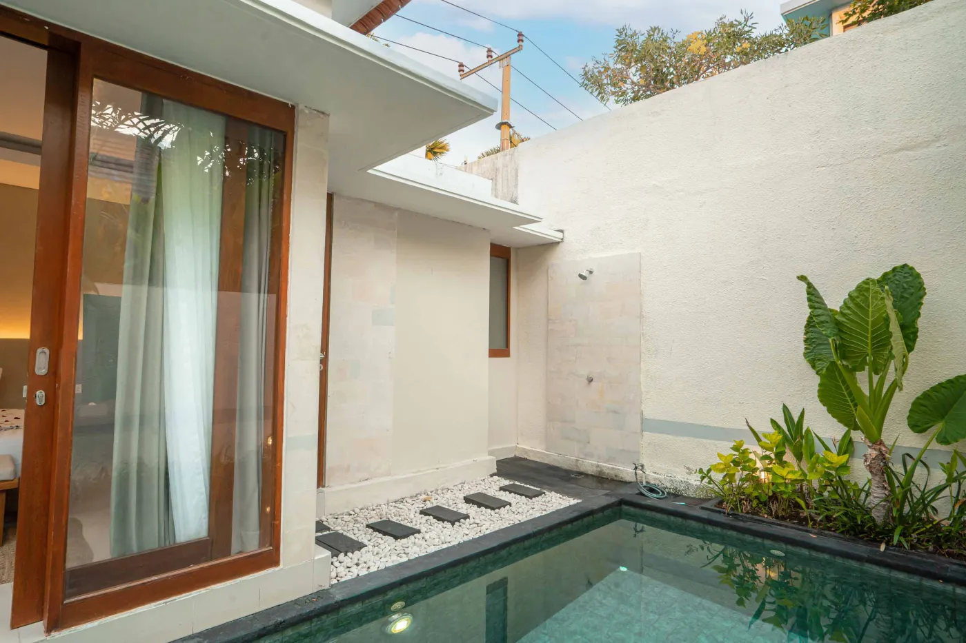Luxurious Bali pool villa with private plunge pool, red bean bag chairs, and open doors to a rose petal-adorned bedroom. - Bali Villas