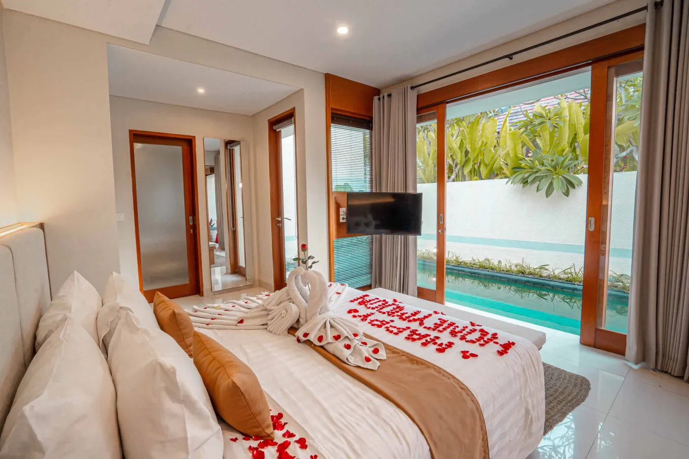 Luxurious Bali pool villa with private plunge pool, red bean bag chairs, and open doors to a rose petal-adorned bedroom. - Bali Villas