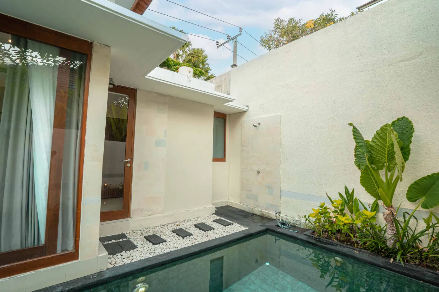 Luxurious Bali pool villa with private plunge pool, red bean bag chairs, and open doors to a rose petal-adorned bedroom. - Bali Villas