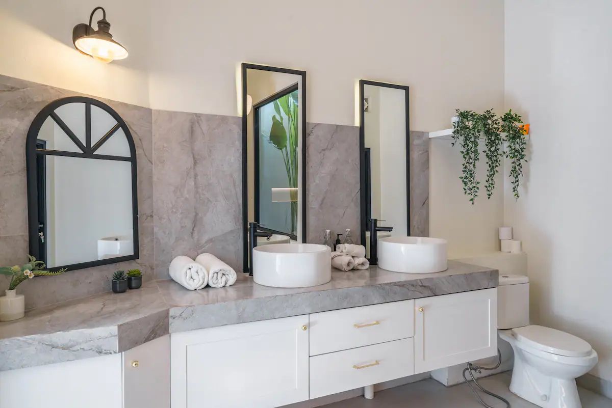 Modern kitchen and dining area in a tropical home, featuring rattan pendant lights, wooden table with chairs, and sliding glass doors to an outdoor pool at dusk. - Bali Villas