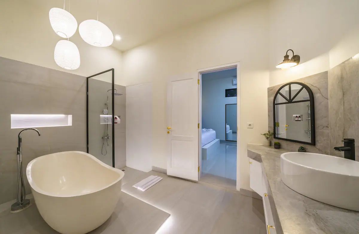 Modern kitchen and dining area in a tropical home, featuring rattan pendant lights, wooden table with chairs, and sliding glass doors to an outdoor pool at dusk. - Bali Villas