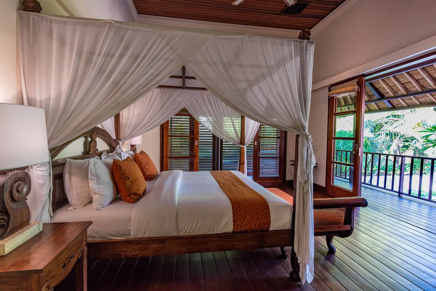Luxurious tropical bathroom featuring a freestanding white bathtub, wooden vanity with double sinks, large mirror, and open door to lush greenery. - Bali Villas