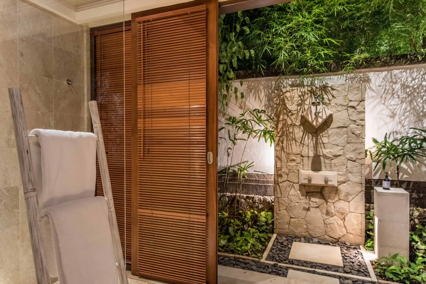 Luxurious tropical bathroom featuring a freestanding white bathtub, wooden vanity with double sinks, large mirror, and open door to lush greenery. - Bali Villas