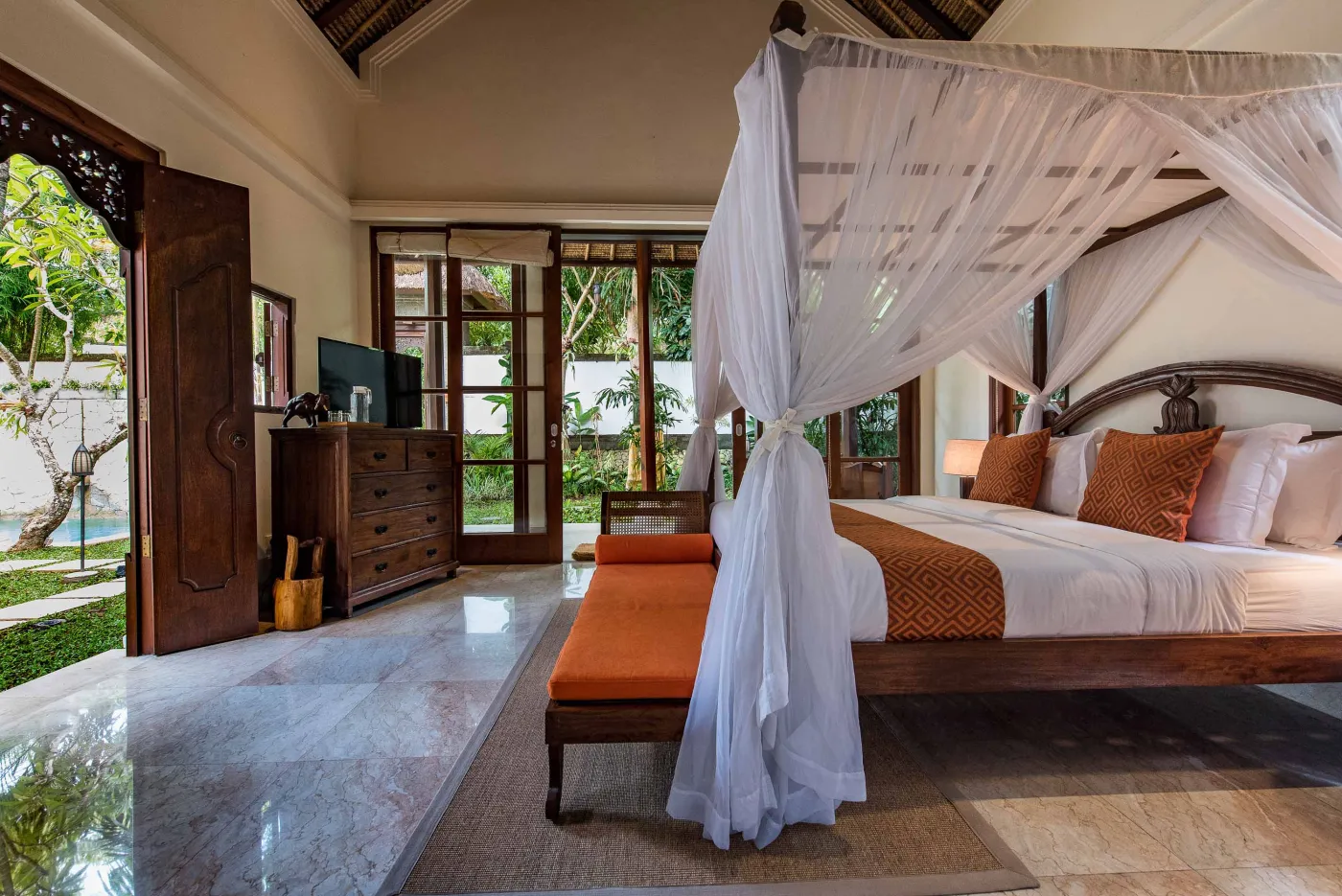Luxurious tropical bathroom featuring a freestanding white bathtub, wooden vanity with double sinks, large mirror, and open door to lush greenery. - Bali Villas