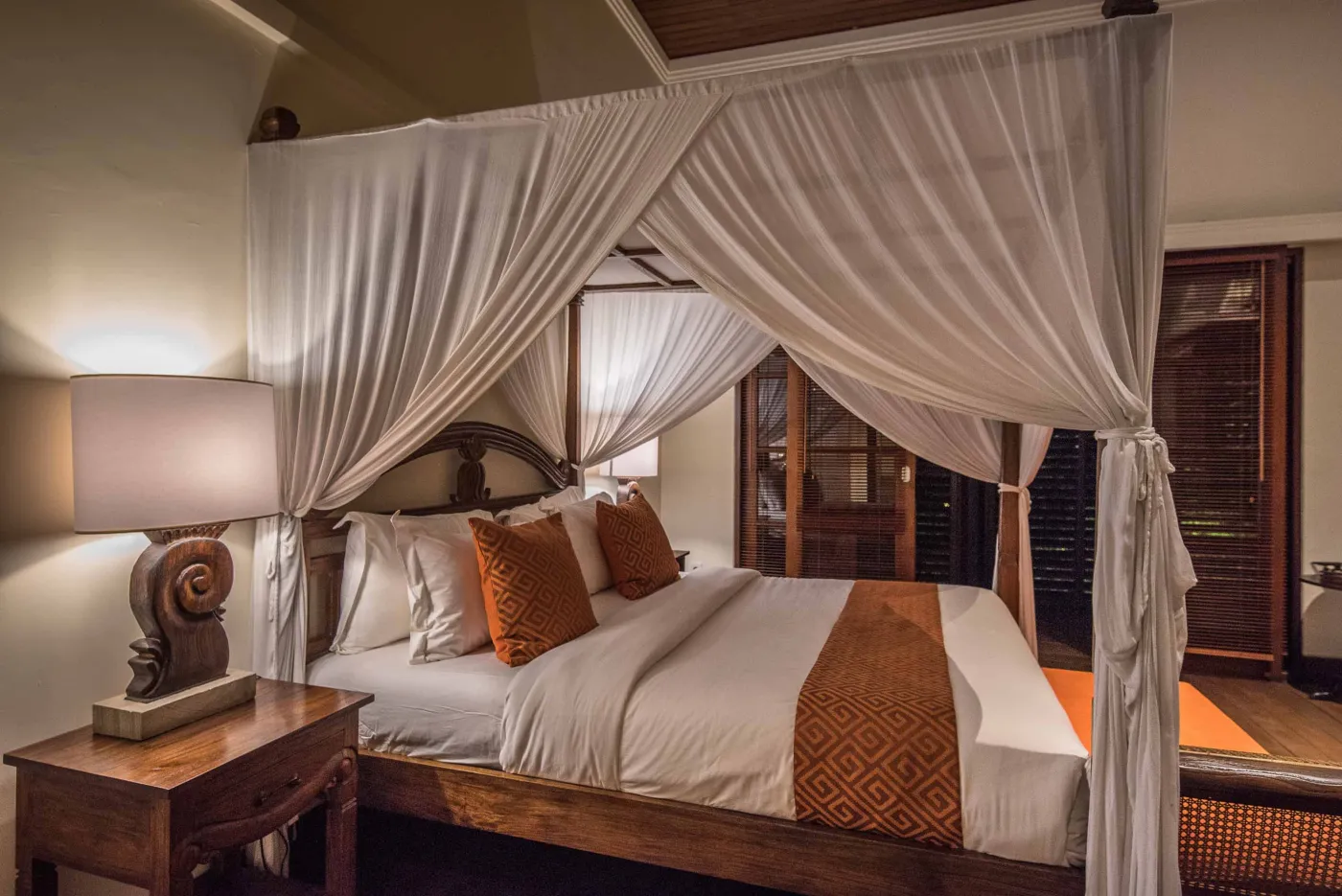 Luxurious tropical bathroom featuring a freestanding white bathtub, wooden vanity with double sinks, large mirror, and open door to lush greenery. - Bali Villas