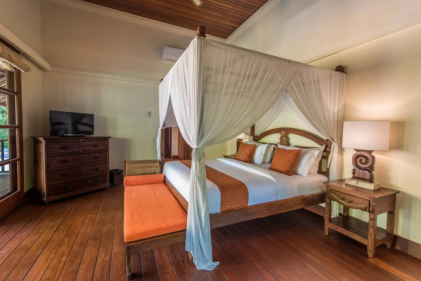 Luxurious tropical bathroom featuring a freestanding white bathtub, wooden vanity with double sinks, large mirror, and open door to lush greenery. - Bali Villas