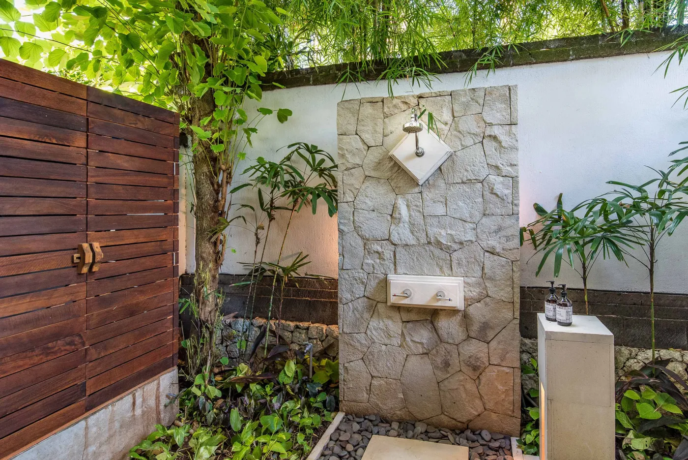 Luxurious tropical bathroom featuring a freestanding white bathtub, wooden vanity with double sinks, large mirror, and open door to lush greenery. - Bali Villas