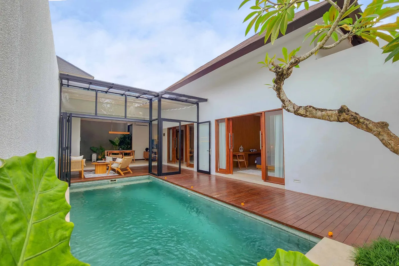 Modern luxury bathroom featuring a freestanding white bathtub, wooden vanity with towels and plants, and bamboo towel rack against neutral walls. - Bali Villas