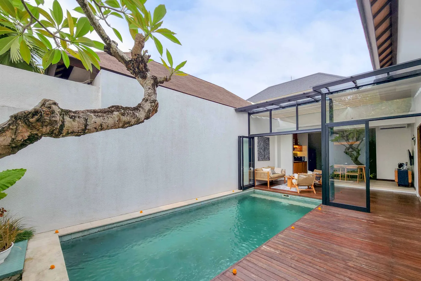 Modern luxury bathroom featuring a freestanding white bathtub, wooden vanity with towels and plants, and bamboo towel rack against neutral walls. - Bali Villas