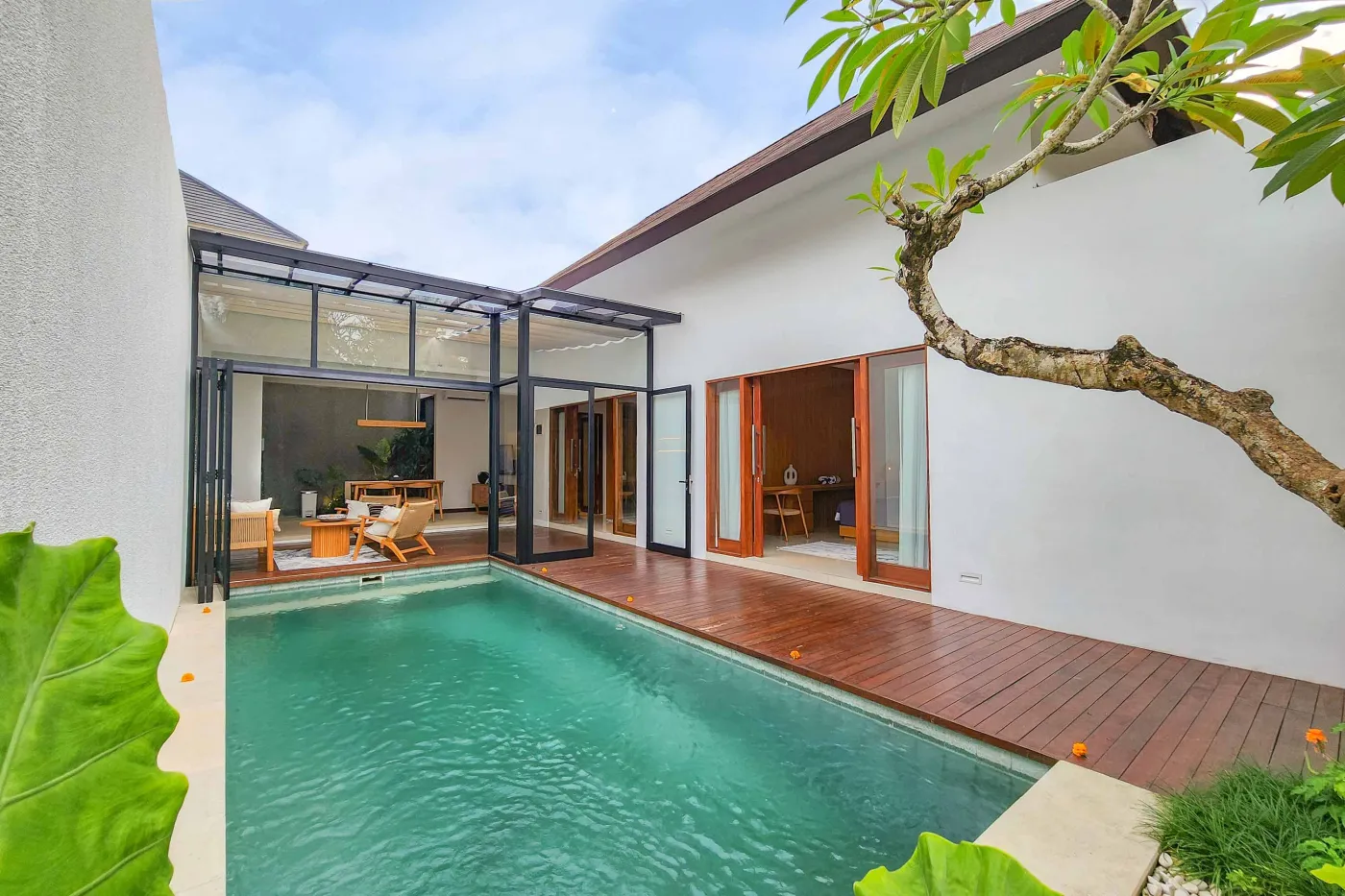 Modern luxury bathroom featuring a freestanding white bathtub, wooden vanity with towels and plants, and bamboo towel rack against neutral walls. - Bali Villas