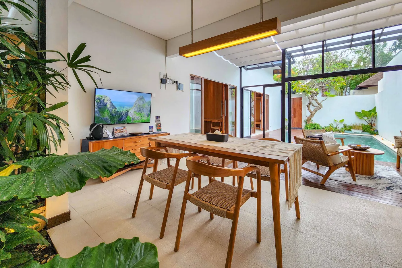 Modern luxury bathroom featuring a freestanding white bathtub, wooden vanity with towels and plants, and bamboo towel rack against neutral walls. - Bali Villas