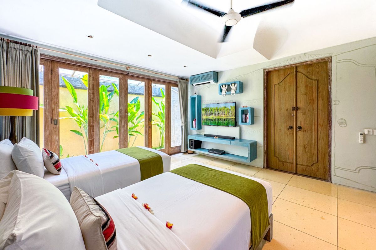 Serene open-air Balinese bathroom featuring a green freestanding bathtub with pink rose petals, tropical plants, and intricate carved wall panels. - Bali Villas