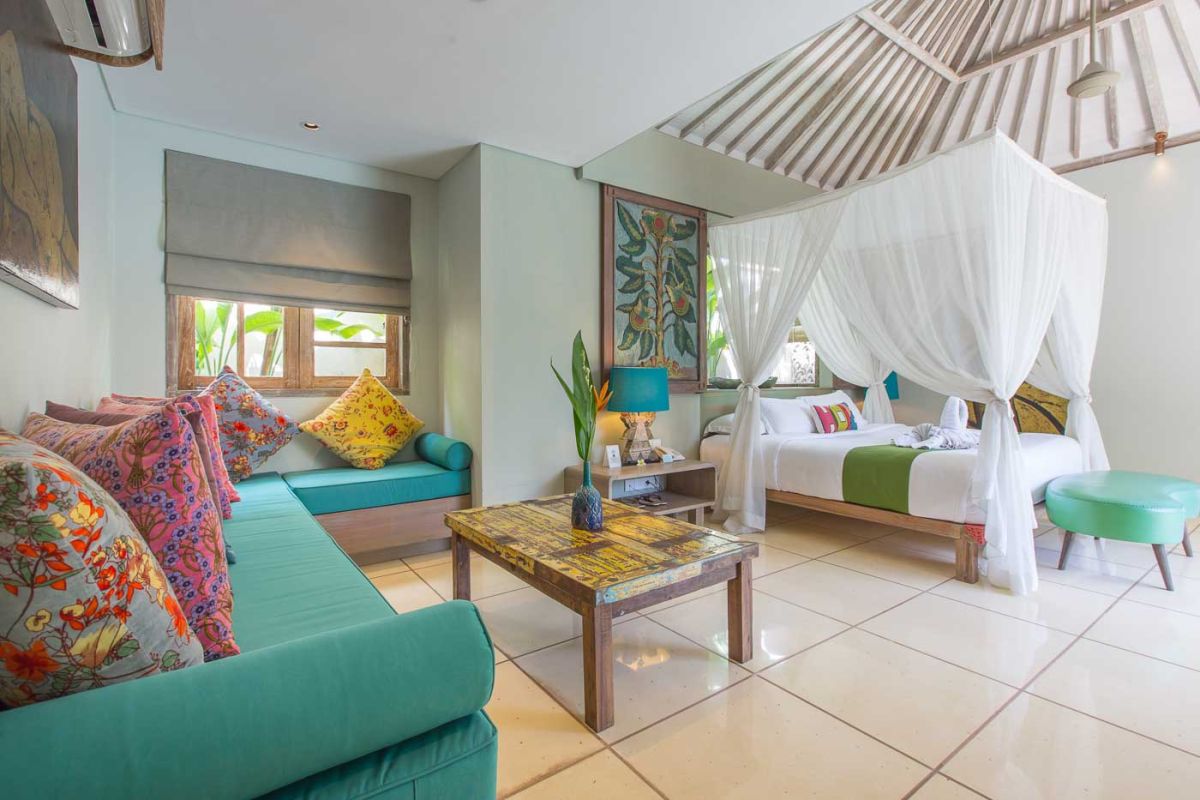 Serene open-air Balinese bathroom featuring a green freestanding bathtub with pink rose petals, tropical plants, and intricate carved wall panels. - Bali Villas
