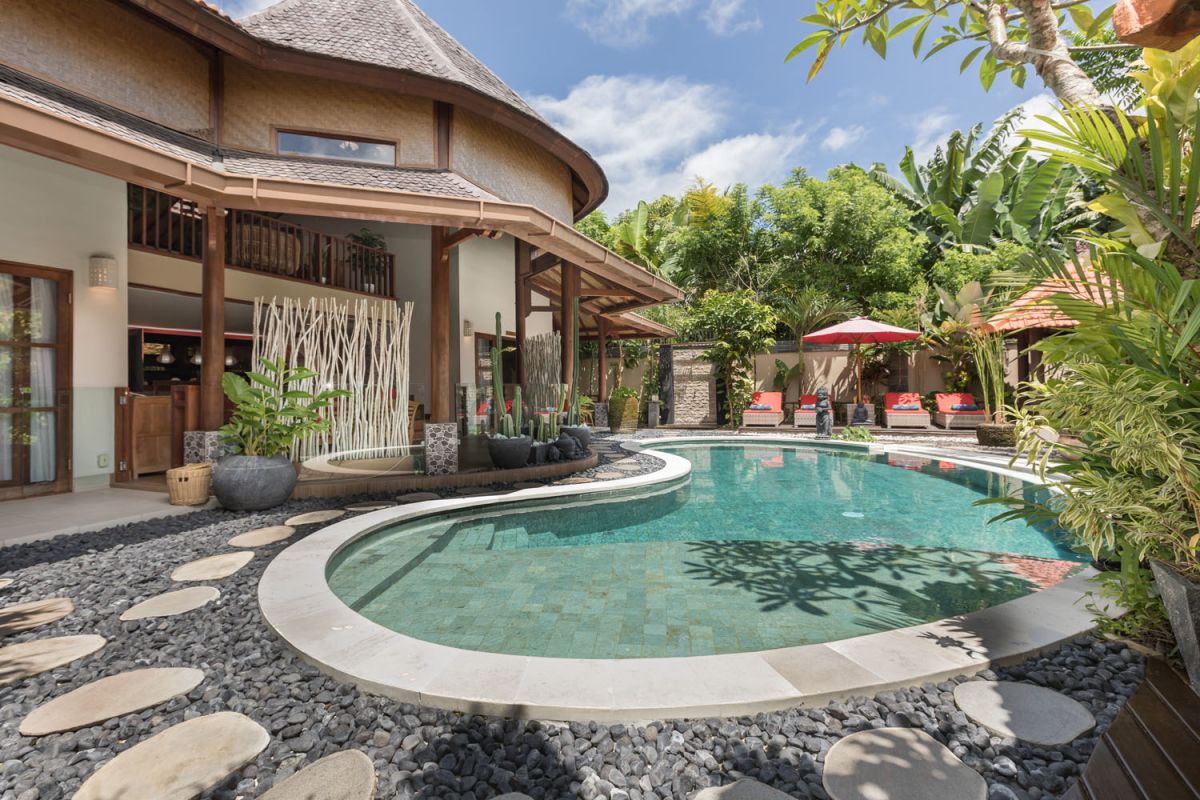 Modern Balinese bathroom with teak wood walls, pebble stone floor, rustic black stone sink, snake plants, and woven accents. - Bali Villas