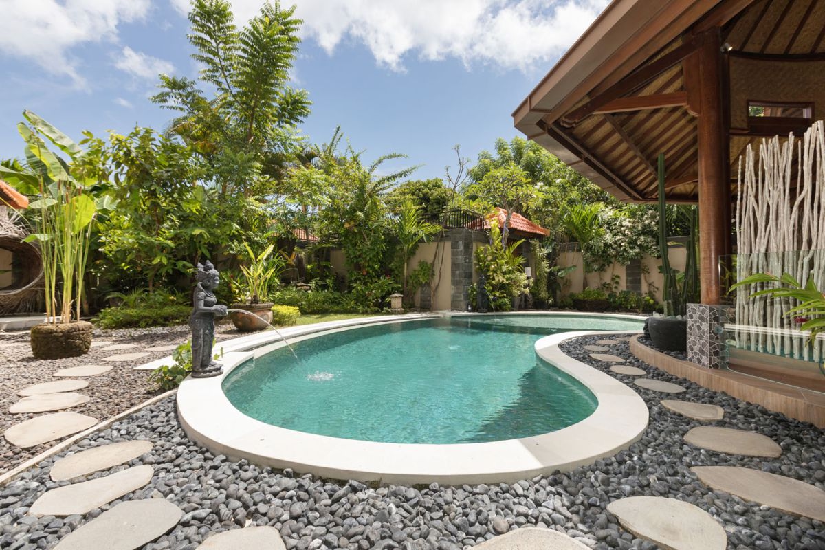 Modern Balinese bathroom with teak wood walls, pebble stone floor, rustic black stone sink, snake plants, and woven accents. - Bali Villas