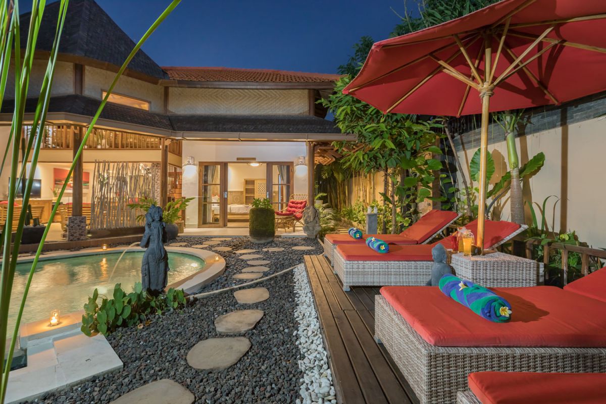 Modern Balinese bathroom with teak wood walls, pebble stone floor, rustic black stone sink, snake plants, and woven accents. - Bali Villas