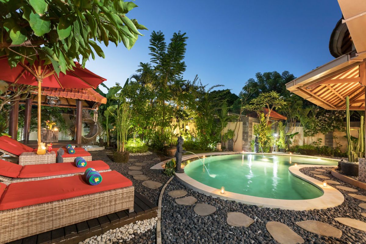 Modern Balinese bathroom with teak wood walls, pebble stone floor, rustic black stone sink, snake plants, and woven accents. - Bali Villas