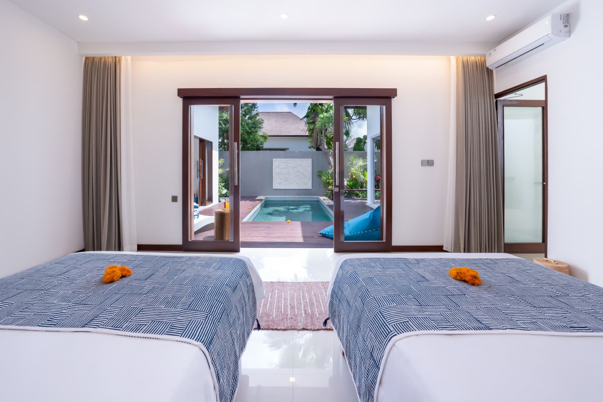 Modern luxury bathroom with soaking tub filled with water and lotus flowers, glass shower enclosure, tropical plants, and natural stone vanity. - Bali Villas