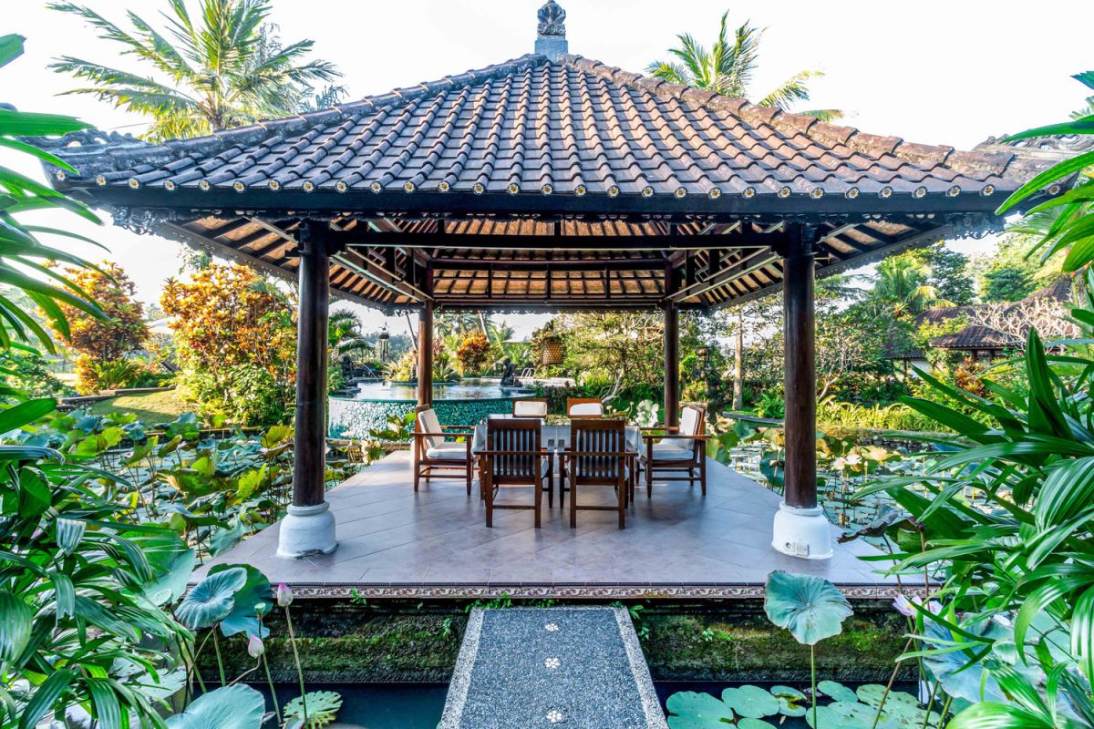 Spacious open-air Balinese pavilion restaurant with thatched roof, wooden tables set for dining, and lush tropical greenery. - Bali Villas