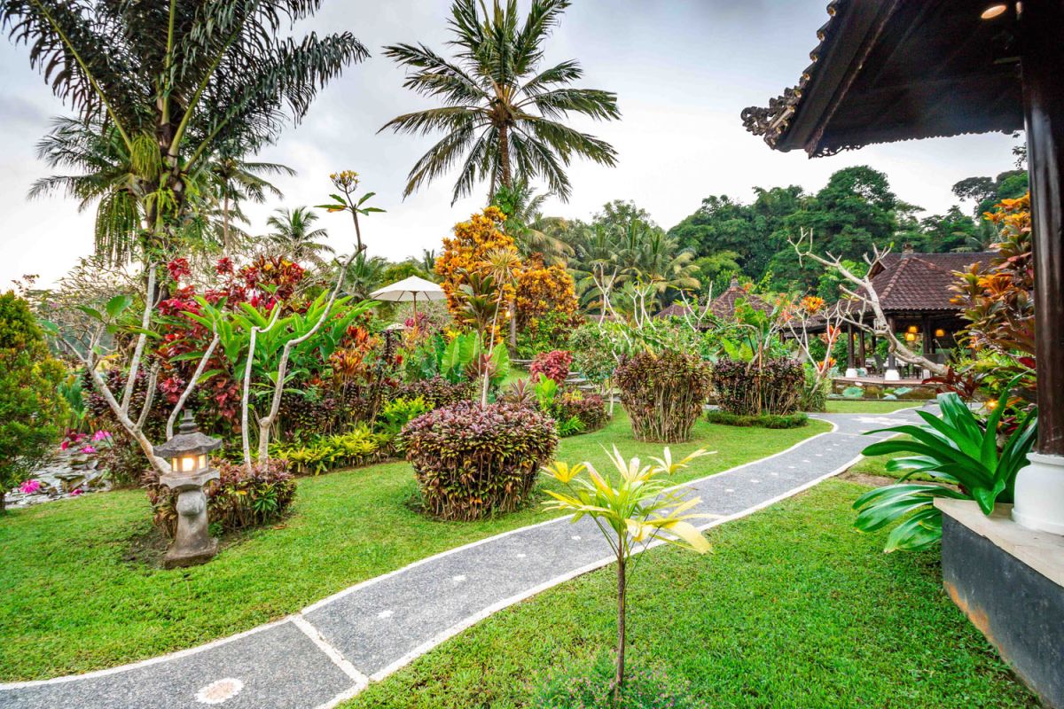 Spacious open-air Balinese pavilion restaurant with thatched roof, wooden tables set for dining, and lush tropical greenery. - Bali Villas