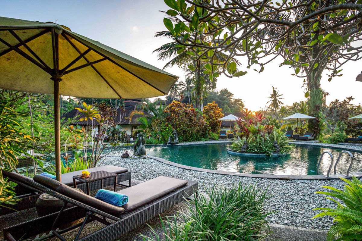 Spacious open-air Balinese pavilion restaurant with thatched roof, wooden tables set for dining, and lush tropical greenery. - Bali Villas