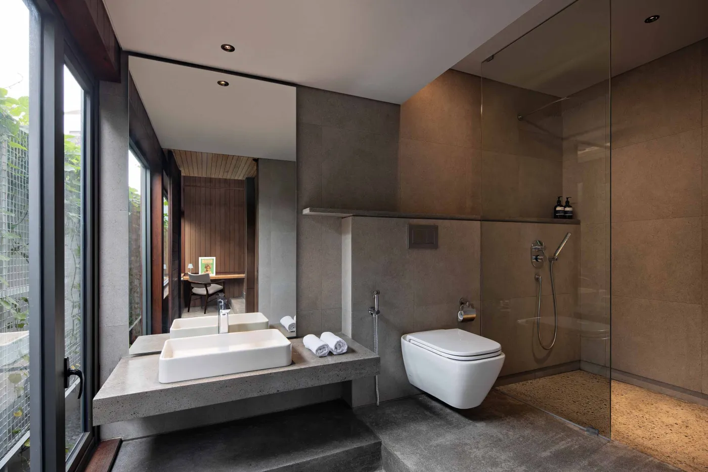 Modern wooden kitchen and dining area with pendant lights, long table set with bowl and runner, and large frosted windows overlooking greenery. - Bali Villas