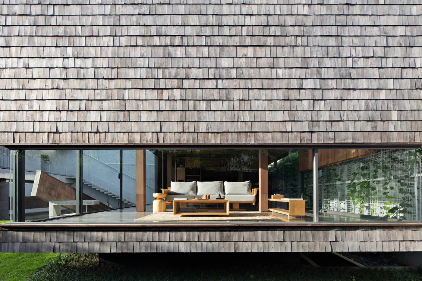 Modern wooden kitchen and dining area with pendant lights, long table set with bowl and runner, and large frosted windows overlooking greenery. - Bali Villas