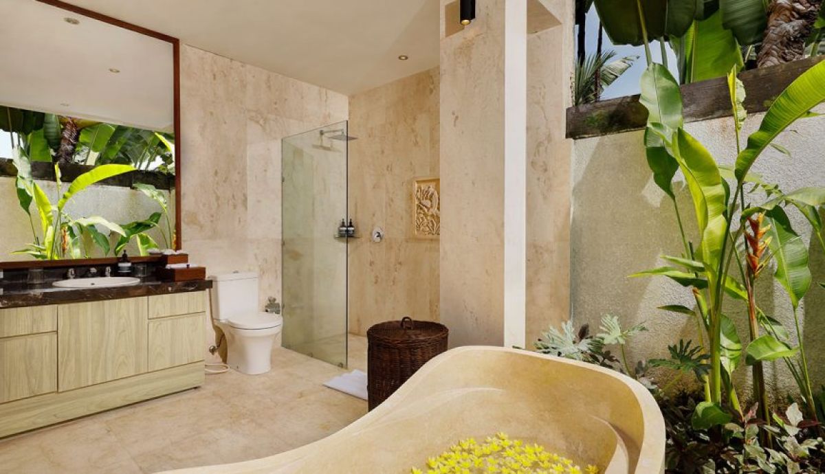 Luxurious Balinese bathroom with flower-petaled freestanding tub, tropical plants, stone walls, and open shower. - Bali Villas