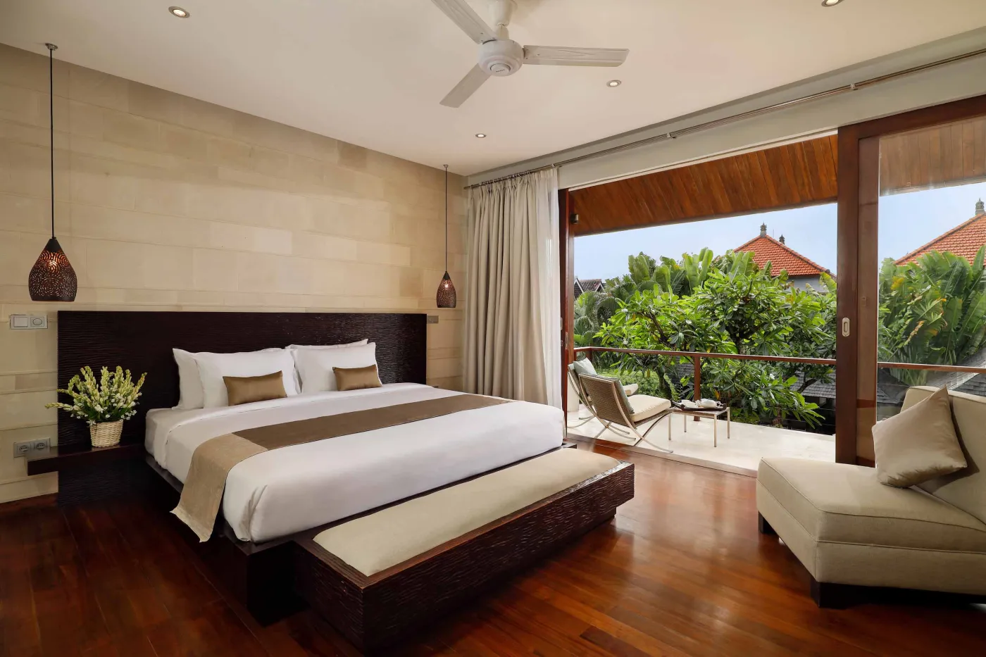Luxurious Balinese-style bathroom featuring a petal-filled freestanding bathtub, glass shower, wooden vanity, and lush tropical plants. - Bali Villas