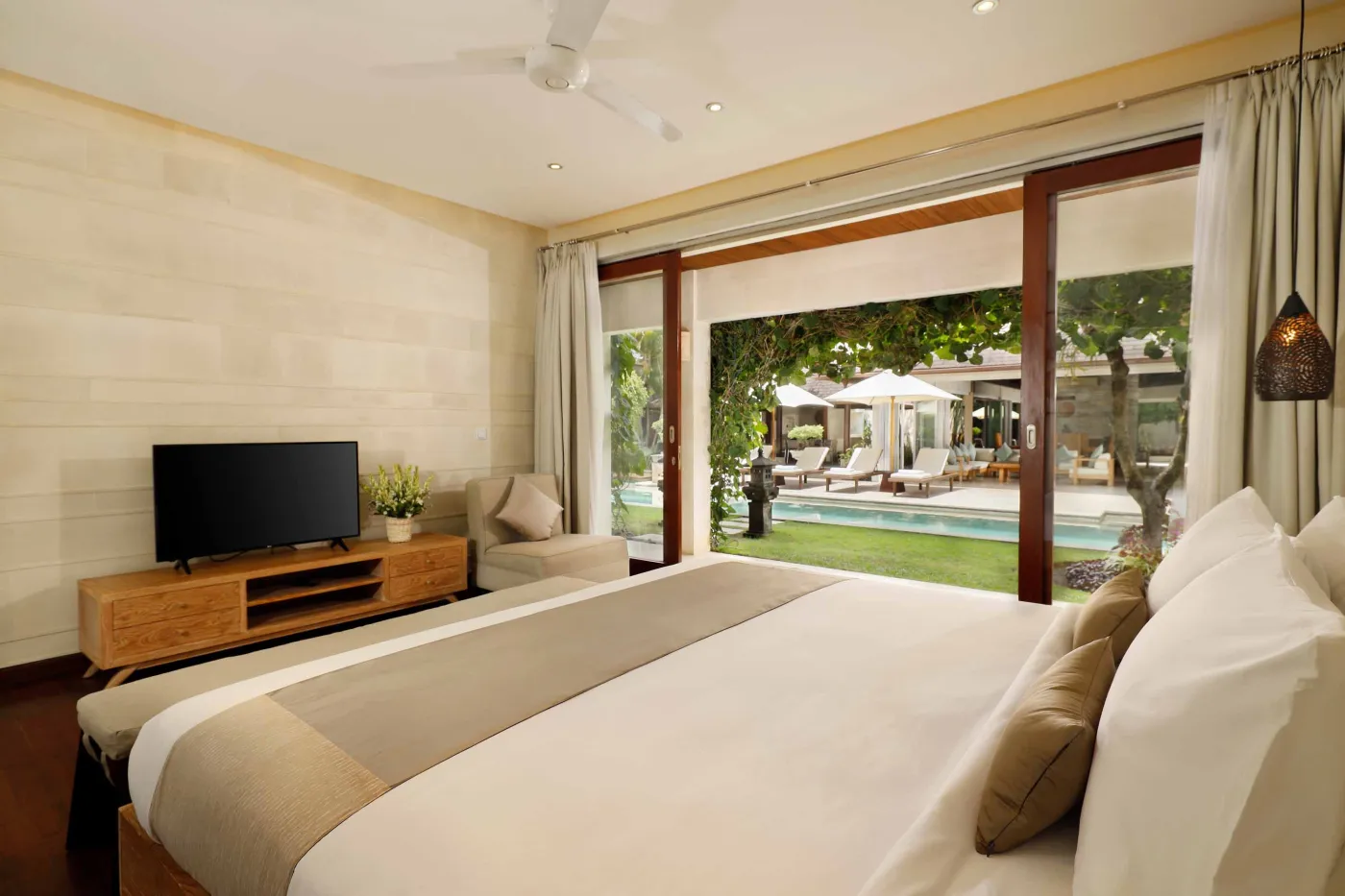 Luxurious Balinese-style bathroom featuring a petal-filled freestanding bathtub, glass shower, wooden vanity, and lush tropical plants. - Bali Villas