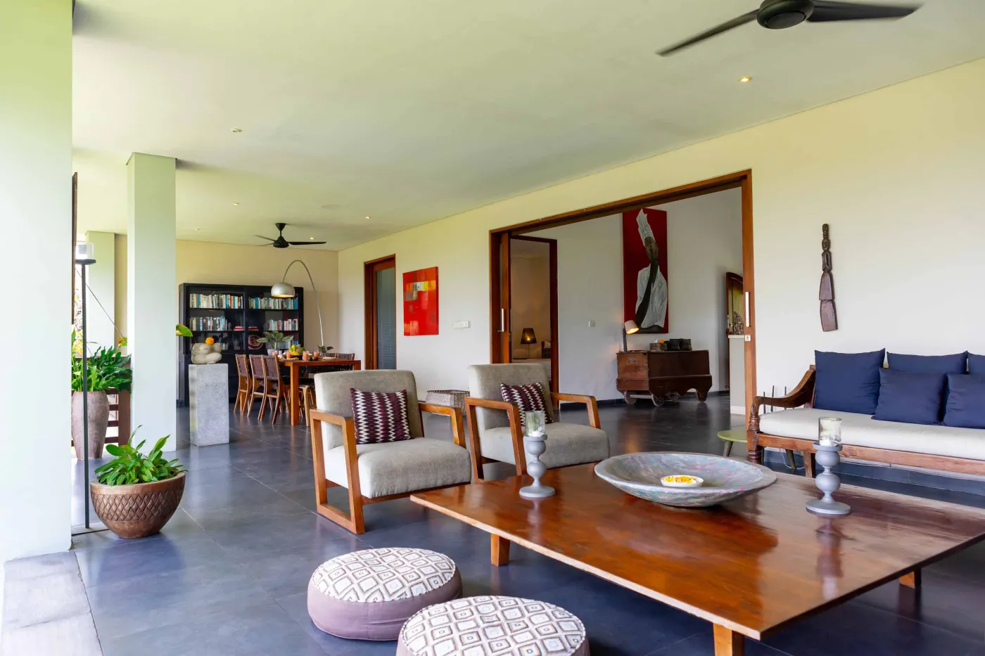 Modern Bali villa living room with purple walls, black-and-white portrait artwork, wooden sofa and coffee table, opening to lush tropical garden and pool. - Bali Villas