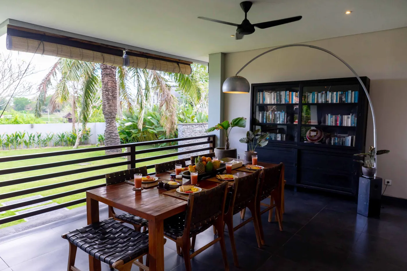 Modern Bali villa living room with purple walls, black-and-white portrait artwork, wooden sofa and coffee table, opening to lush tropical garden and pool. - Bali Villas