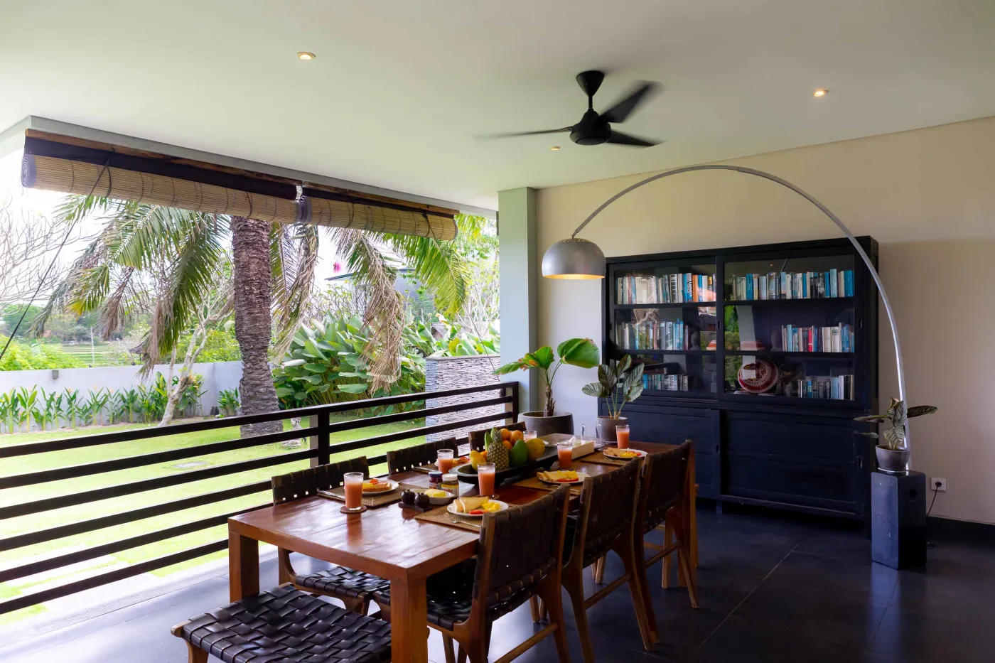 Modern Bali villa living room with purple walls, black-and-white portrait artwork, wooden sofa and coffee table, opening to lush tropical garden and pool. - Bali Villas