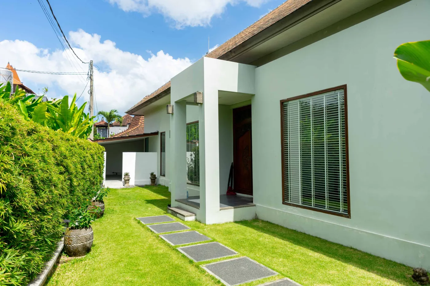 Modern Bali villa living room with purple walls, black-and-white portrait artwork, wooden sofa and coffee table, opening to lush tropical garden and pool. - Bali Villas