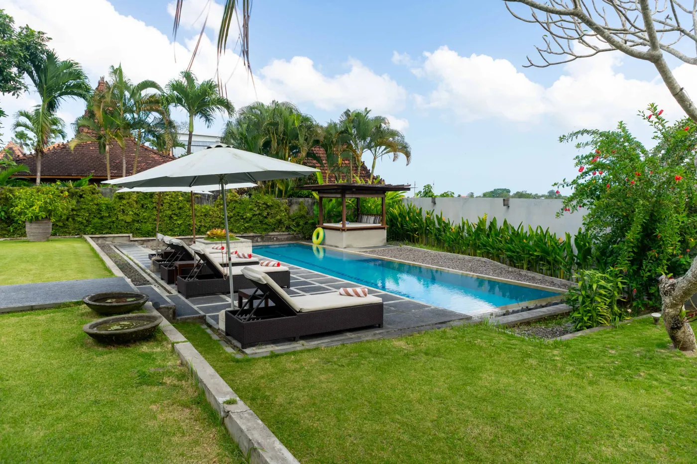 Modern Bali villa living room with purple walls, black-and-white portrait artwork, wooden sofa and coffee table, opening to lush tropical garden and pool. - Bali Villas