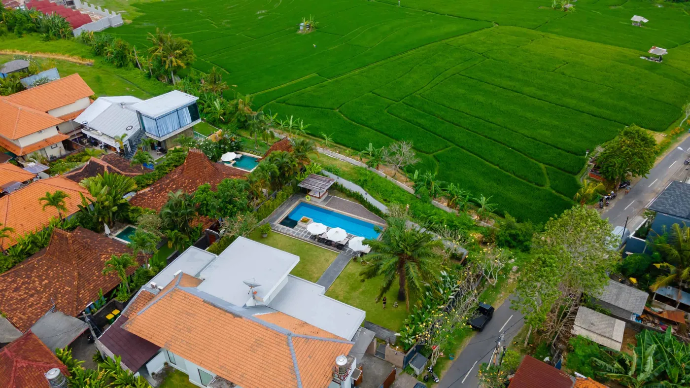 Modern Bali villa living room with purple walls, black-and-white portrait artwork, wooden sofa and coffee table, opening to lush tropical garden and pool. - Bali Villas
