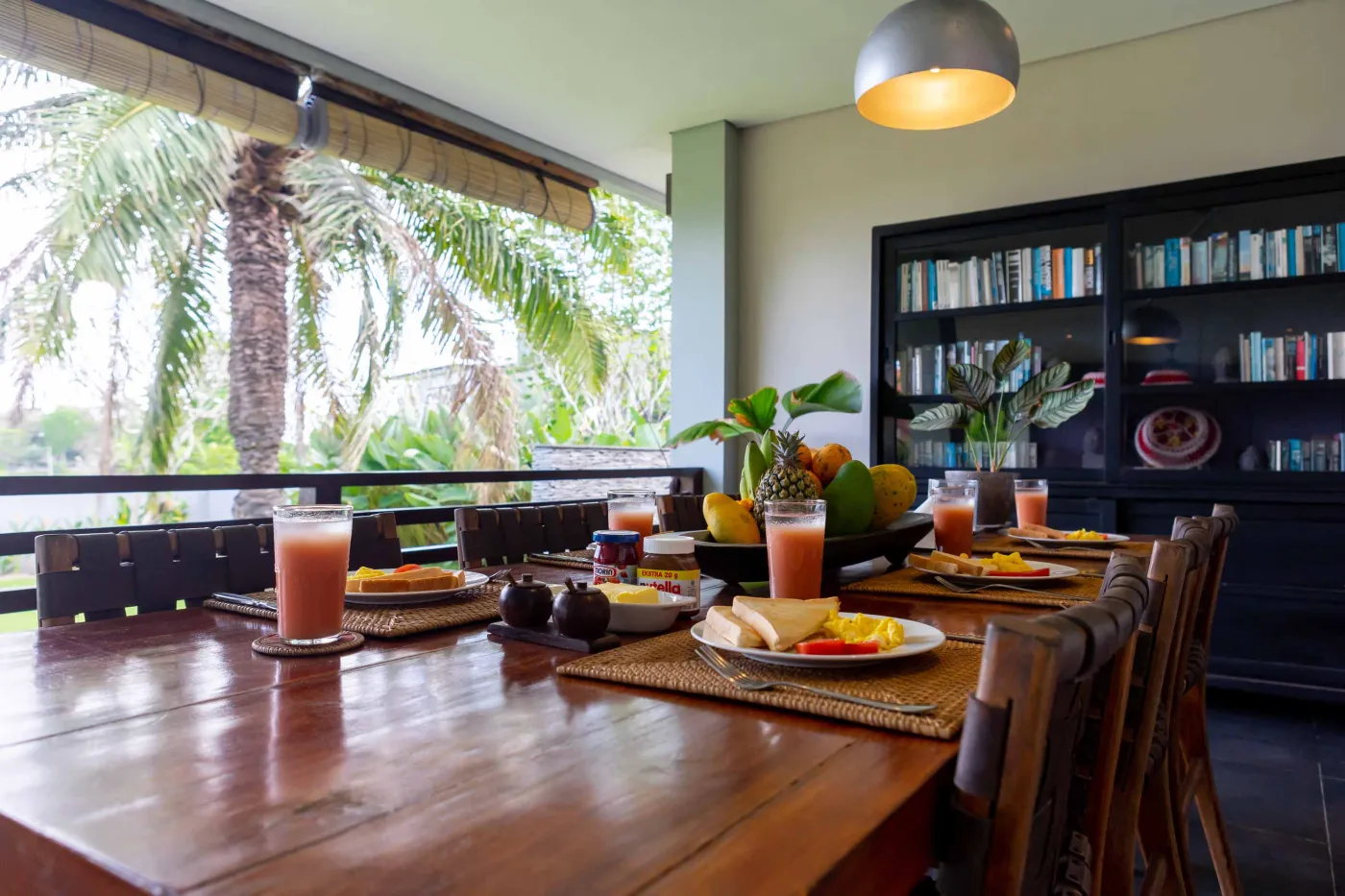 Modern Bali villa living room with purple walls, black-and-white portrait artwork, wooden sofa and coffee table, opening to lush tropical garden and pool. - Bali Villas