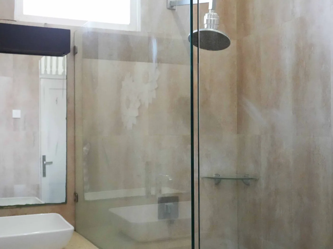 Modern bathroom with glass shower enclosure, rain showerhead, and wooden vanity sink. - Bali Villas