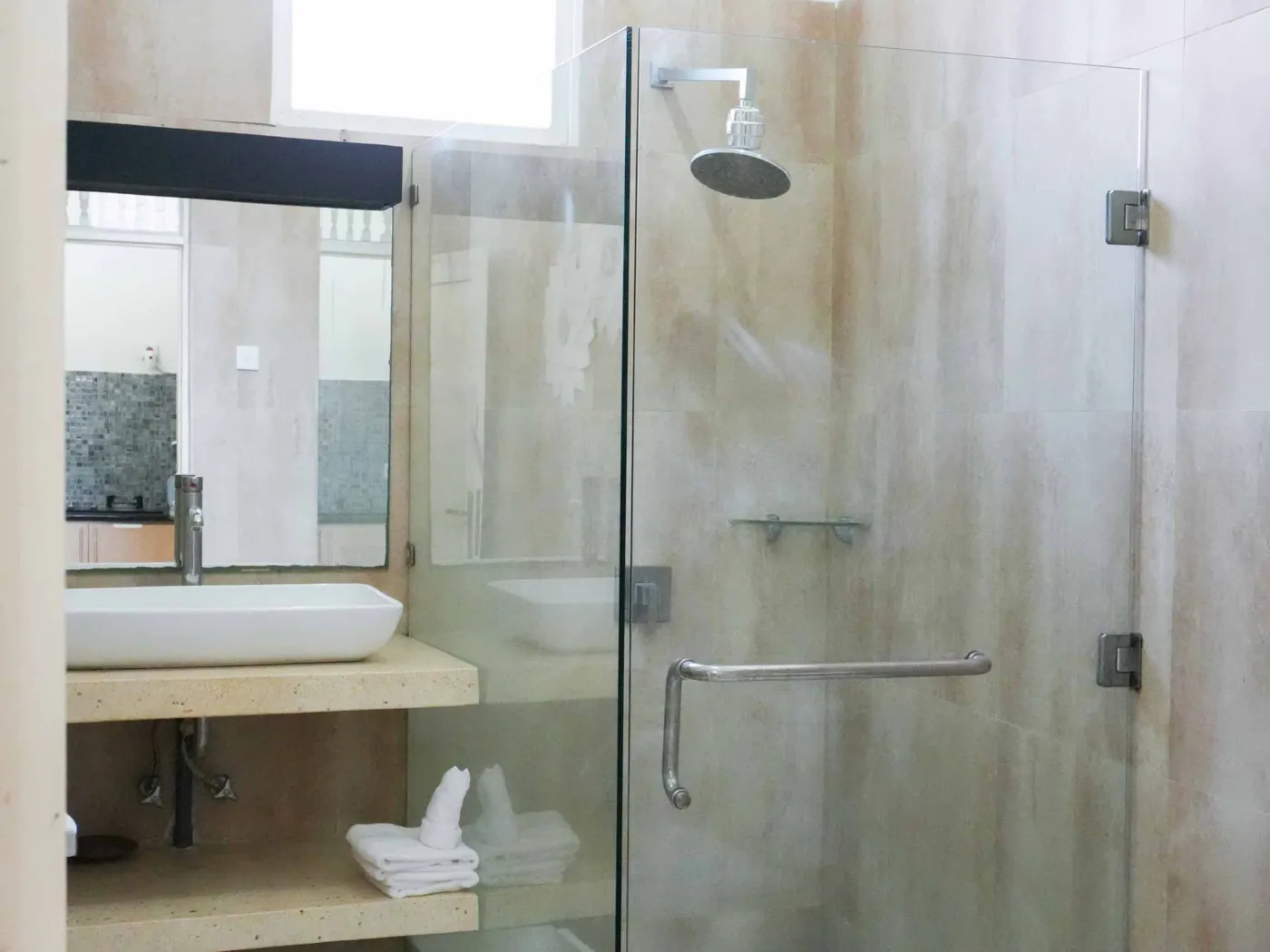 Modern bathroom with glass shower enclosure, rain showerhead, and wooden vanity sink. - Bali Villas