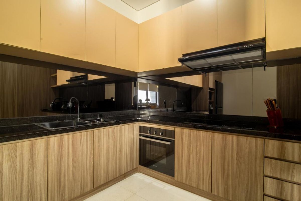 Modern open-plan living room with wooden TV cabinet, beige sofas, rustic coffee table, chandelier, and visible kitchen area. - Bali Villas
