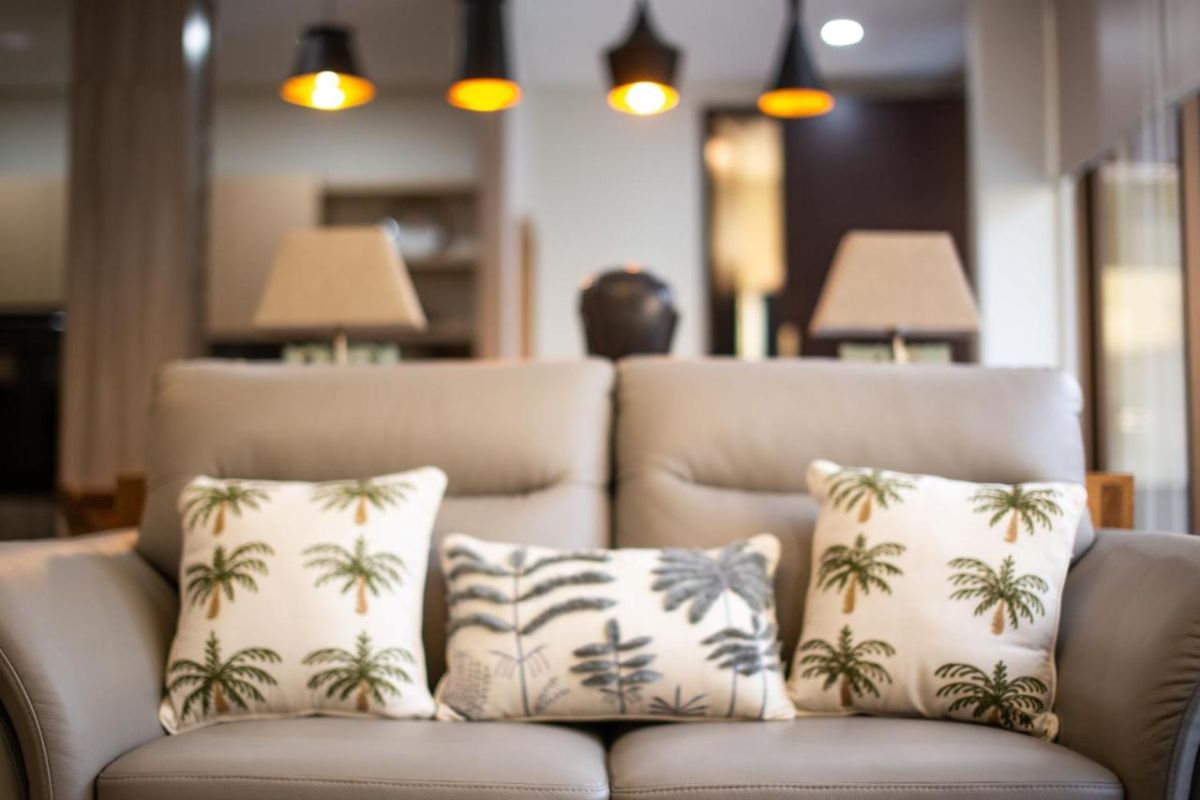 Modern open-plan living room with wooden TV cabinet, beige sofas, rustic coffee table, chandelier, and visible kitchen area. - Bali Villas