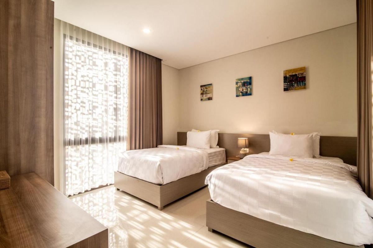 Modern open-plan living room with wooden TV cabinet, beige sofas, rustic coffee table, chandelier, and visible kitchen area. - Bali Villas