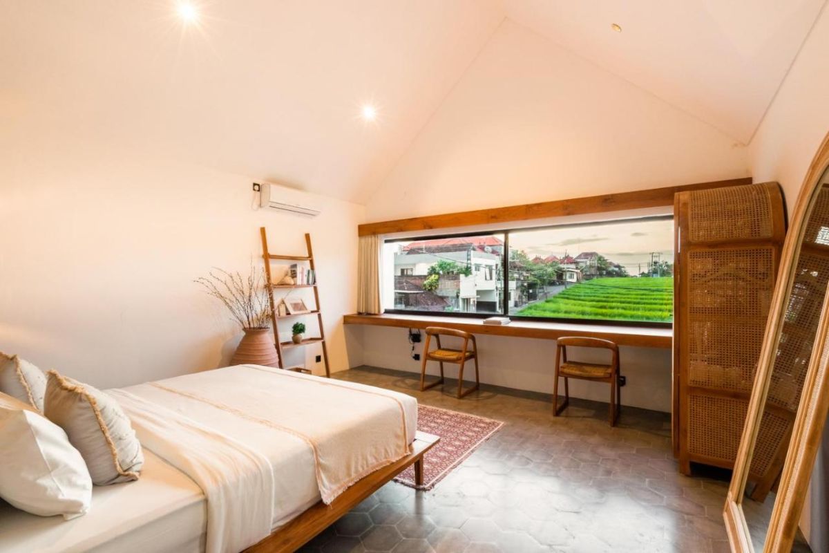 Serene modern bedroom with wooden bed, desk, and large windows overlooking lush green rice fields. - Bali Villas